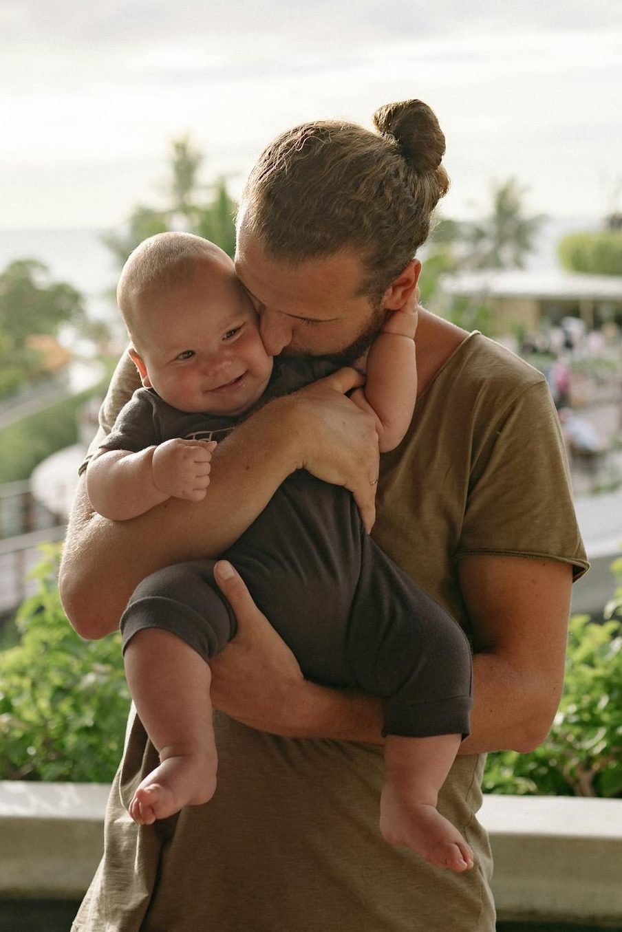 A joyful dad holding his baby with love and warmth outdoors, showcasing fatherhood.