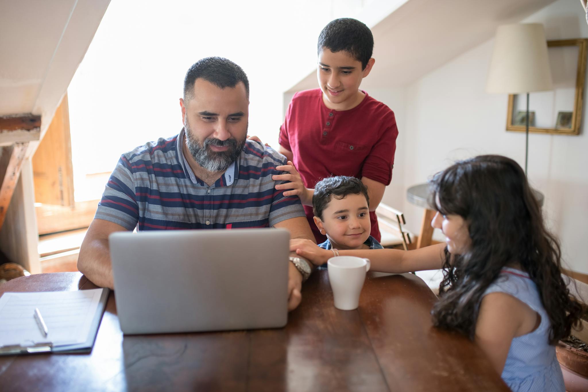 Father working on laptop with kids at home, enjoying quality family time in a cozy indoor setting.